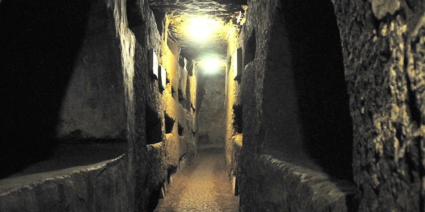 Inside the catacombs of Domitilla with a narrow pathway and carved spaces in the tunnel.