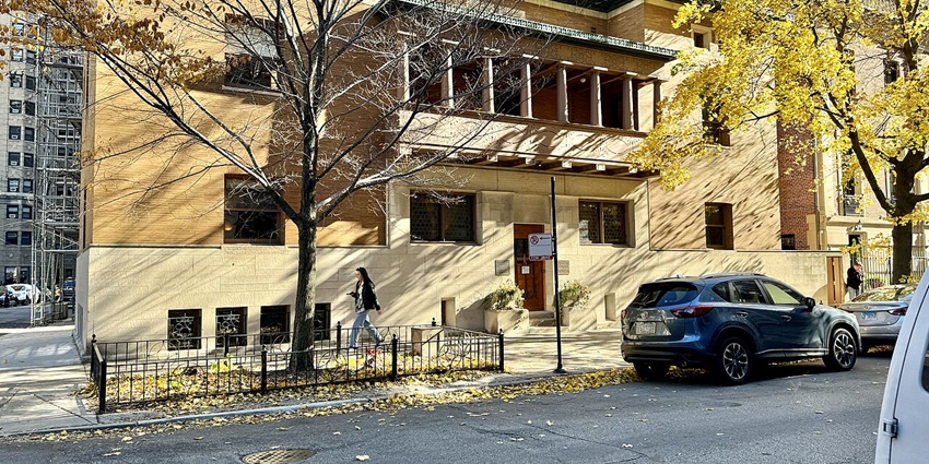 Front of the Charnley house in Chicago with vehicles parked, a signboard and a woman.