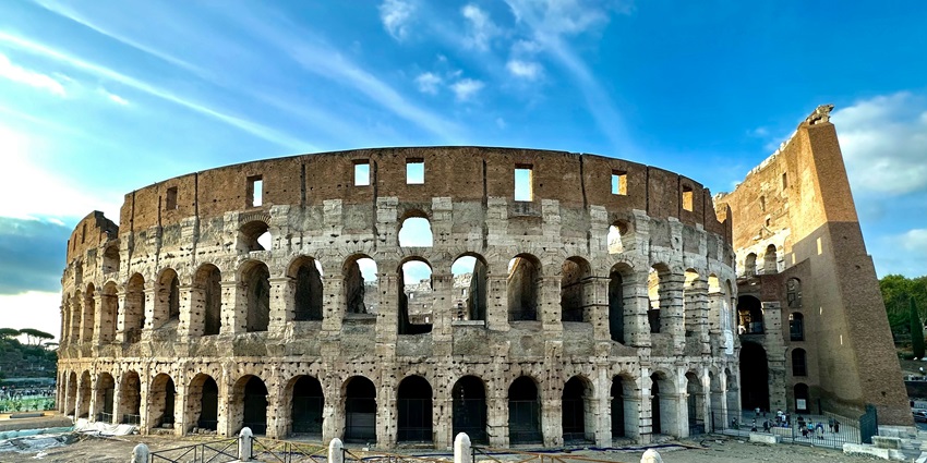 The Colosseum in the evening with ancient architecture, fencing and people visiting.