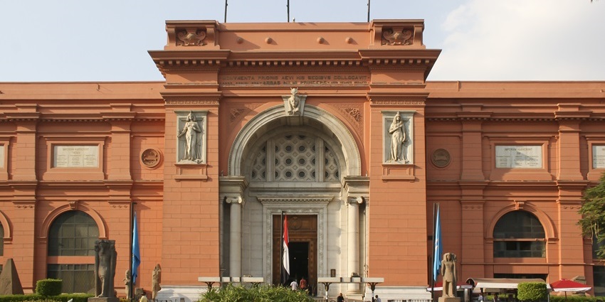 Grand façade of the Egyptian Museum with neoclassical architecture and palm trees.