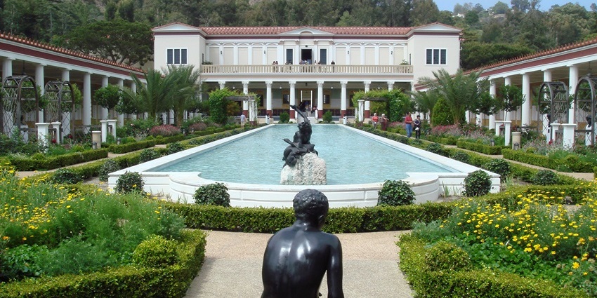 The Getty Villa with white architecture, two detailed black statues, and a small water body