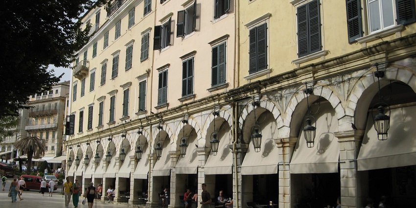 A historic European building with an arched colonnade, shuttered windows, one of the best historical places in Corfu.