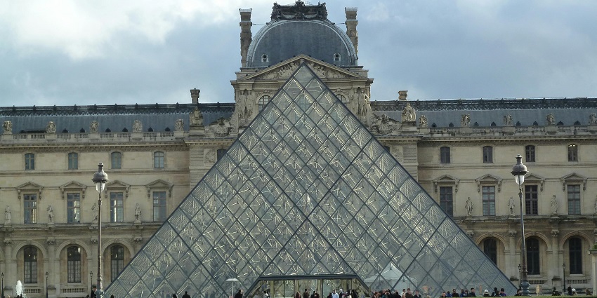 Glass pyramid entrance of the Louvre Museum surrounded by historic palace walls.