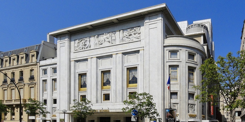 A lovely white building and a few people walking were seen on a bright morning beneath a blue sky.