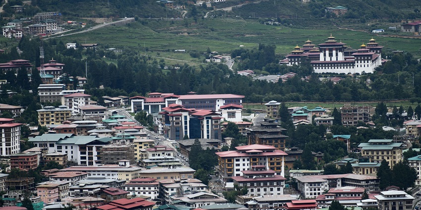 Thimphu city with multiple vibrant buildings & houses, red roofs and tall green trees.
