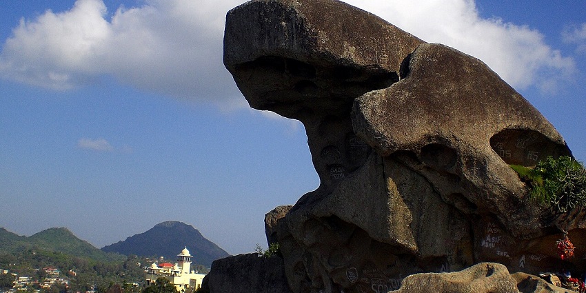 Toad rock at Mount Abu with black stone shaped like a toad, buildings and mountains.