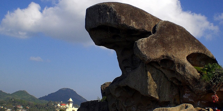 Toad Rock at Mount Abu with green hills and distant houses, amongst the best places to visit in Mount Abu in April