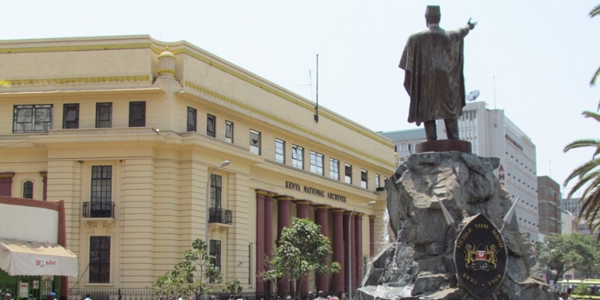 A crowd of visitors gathered around the Tom Mboya Statue in Nairobi on a busy day.
