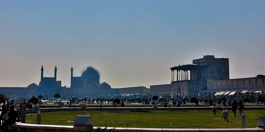 Toopkhaneh Square with distant traditional Islamic monuments, and people sitting
