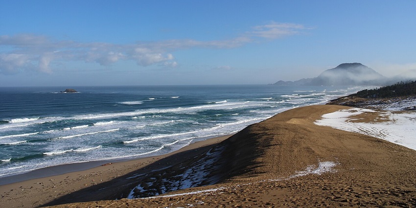 Tottori sand dunes partially covered with snow, sandy shoreline and distant mountains