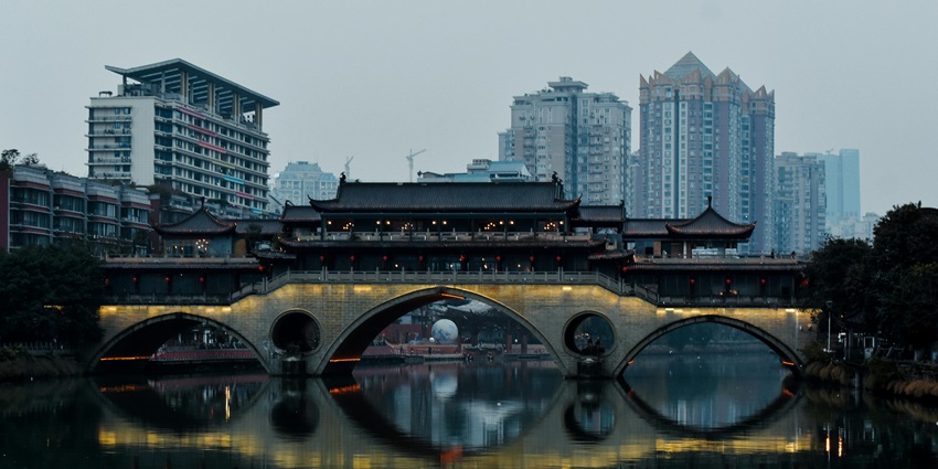 Illuminated Anshun Lang Bridge reflecting over the Jin River, framed by city lights at night.