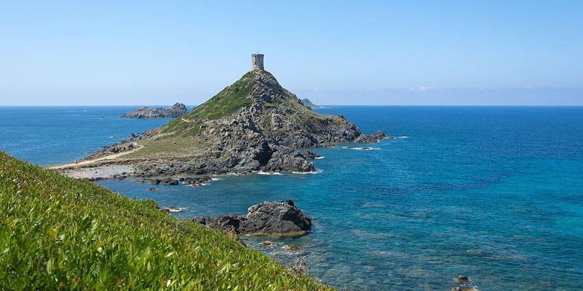 Tour de la Parata on the small green and partially rocky mountain with a distant structure.
