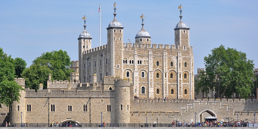 Tower of London from the River Thames with traditional British architecture and a flag on top.