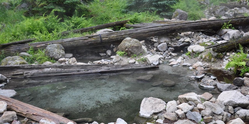 Stanley Hot Springs with small hot water pond, wood logs and surrounded by rocks.