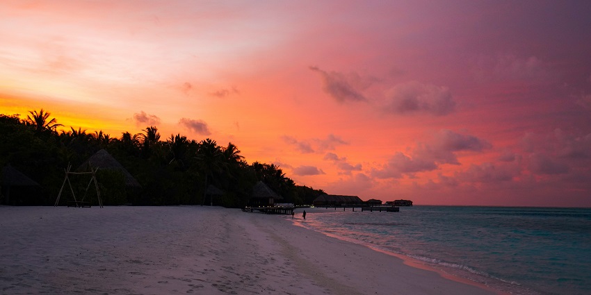 Beach during sunset with glowing sky, gentle waves, and calm, reflective shoreline.