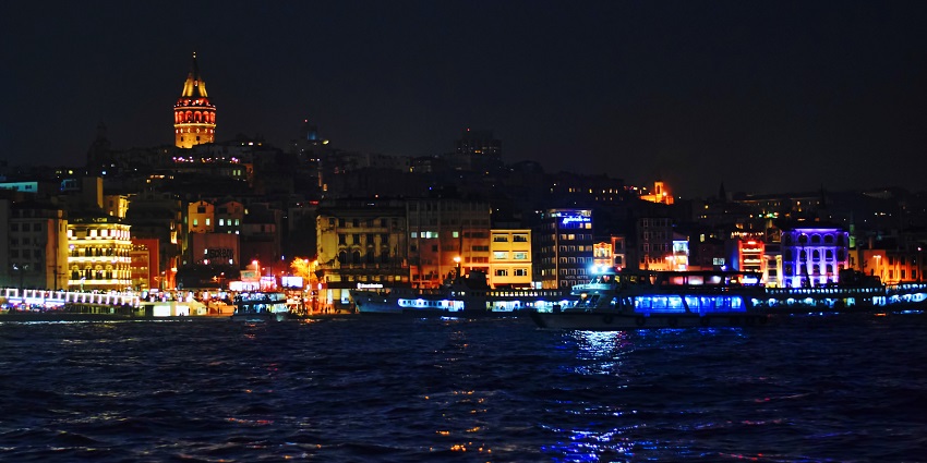 Illuminated night view of a Turkish city skyline with glowing buildings and quiet streets.