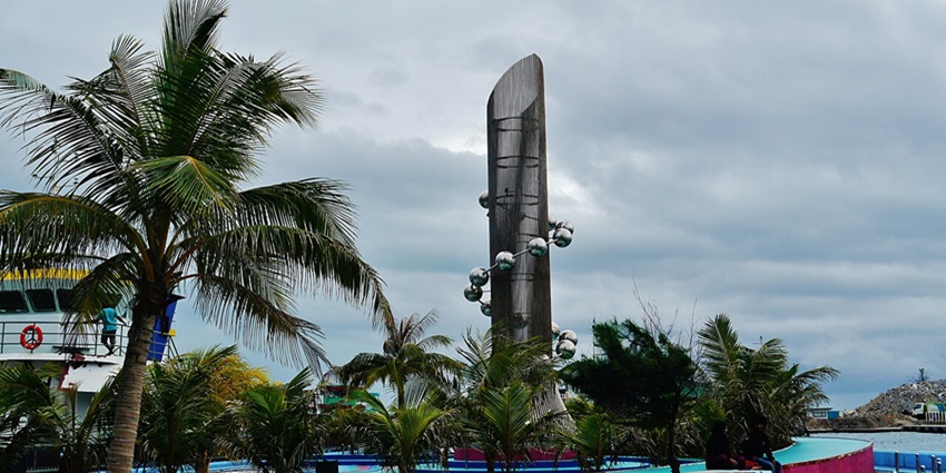 Tsunami monument in Malé with unique architecture, a distant man standing and palm trees
