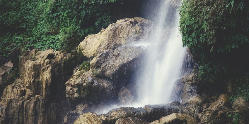 Tegenungan waterfall with multiple people sitting on the rocky cliff near the waterfall.