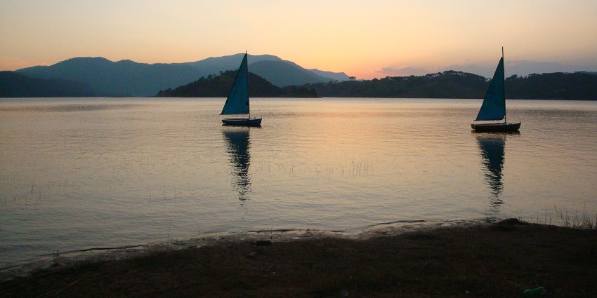 Umiam Lake in the evening with still water body, two boats in the lake and mountains, one of the best places to visit in Shillong in July.