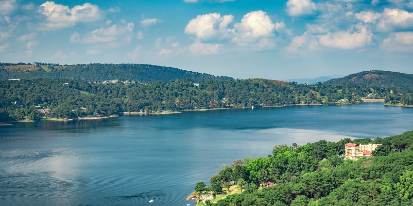 Umiam Lake from above with a large still water body, green mountains and clouds in the sky
