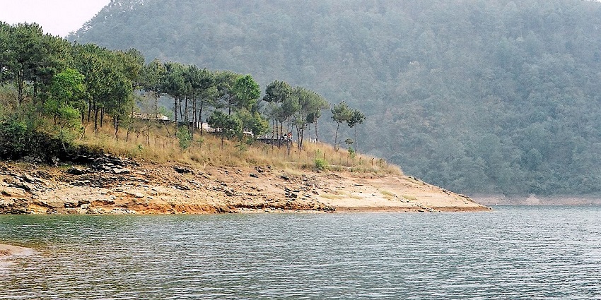 Umiam Lake in Meghalaya with sandy shorelines, green trees and mountains at a distance.