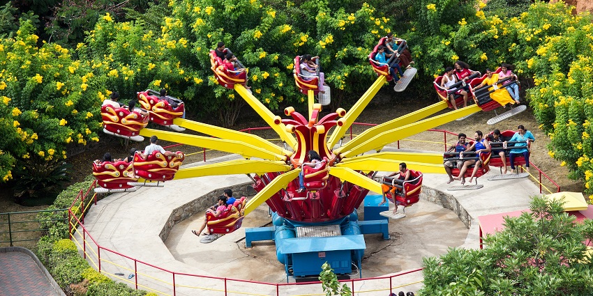 People are enjoying a colourful spinning amusement park ride surrounded by vibrant trees.