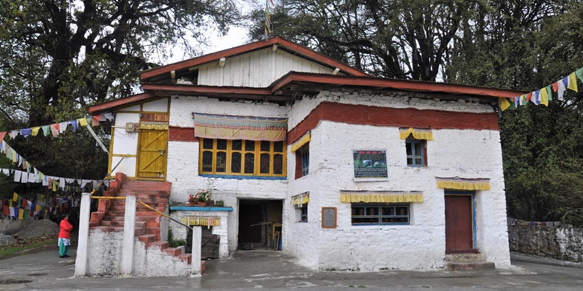 Urgelling monastery with stairs, multiple windows, Tibetan flags and a woman standing