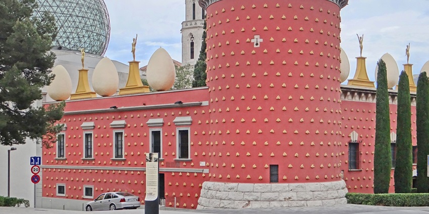 Surreal red façade of the Dalí Theatre-Museum in Figueres with giant eggs and whimsical sculptures.