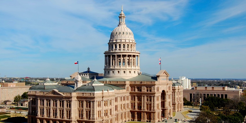 Grand pink granite Texas State Capitol building with a central dome and green lawn in front.