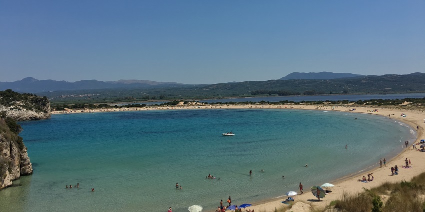 Voidokilia Beach with sandy shorelines, distant people on the beach and hills in the back.