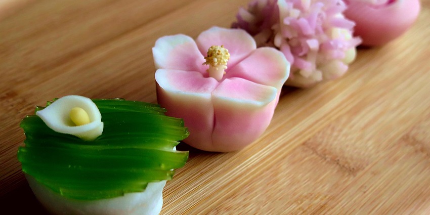 Delicately shaped wagashi sweets in pastel colours placed on a black lacquer tray with leaves.