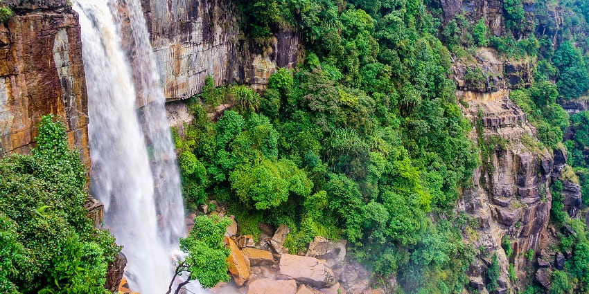 Waterfalls in Meghalaya with water flowing on the rocky surface surrounded by greenery.