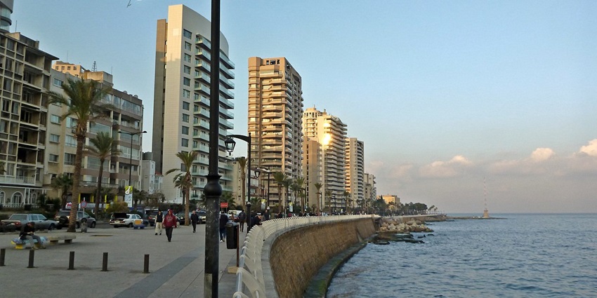 People walking along the scenic Beirut Corniche at sunset with the sea and palm trees.