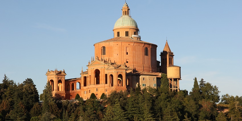 Hilltop church with a large dome and orange façade, surrounded by greenery and distant city views