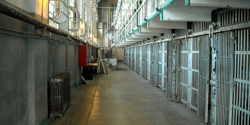 Interior view of the historic cellhouse, featuring narrow prison cells, barred doors, and stark concrete walkways.