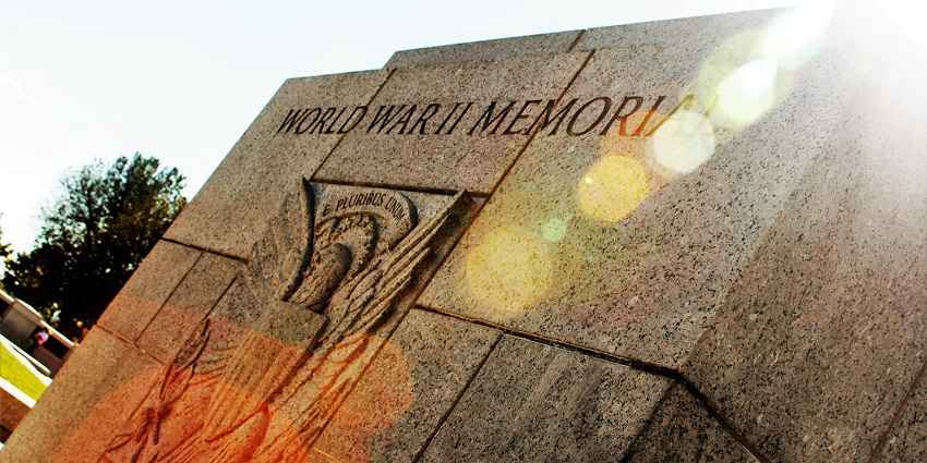 World War II memorial engraved on a rock with a symbol and sunlight creating colours