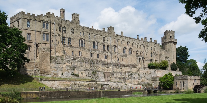 South facade of Warwick Castle with ruined old architecture and people visiting the castle