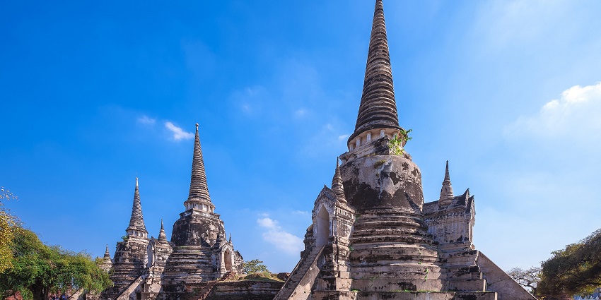 Ancient temple ruins with tall spires under the clear blue sky, one of the top historical places in Thailand.