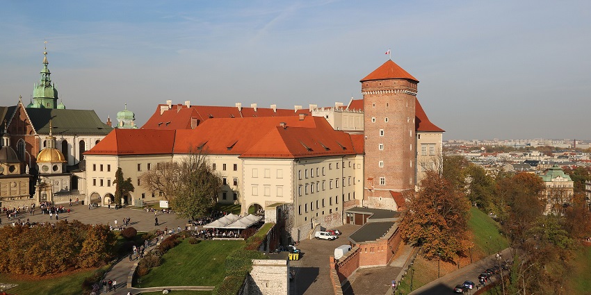 Wawel Royal Castle with orange roofs, a tall tower, a flag on top of the castle and people visiting