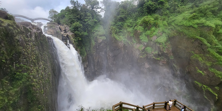 Weinia falls in west Khasi Hills with green grass on the rocks and people standing.