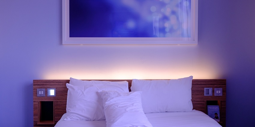 Cosy hotel bedroom with neatly made bed, soft sheets, and warm ambient lighting.