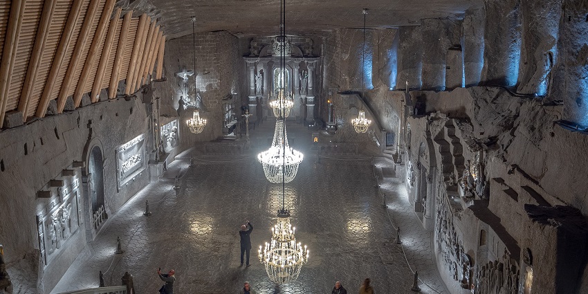 Wieliczka Salt Mine with multiple fancy hanging lights, people visiting and intricate carvings