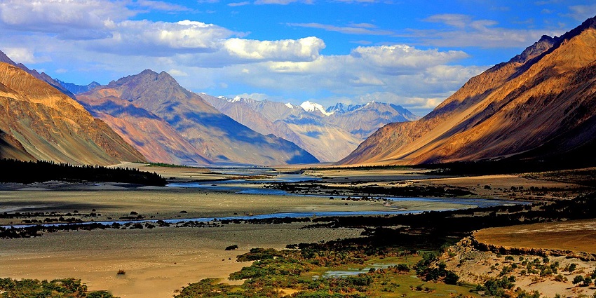 Remote Himalayan valley with snow-covered peaks, trekking routes, and river rafting adventures.
