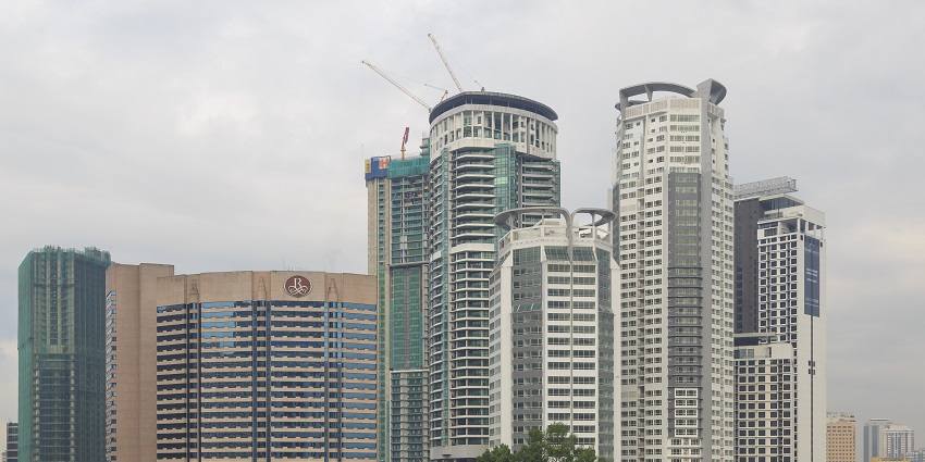 Tall buildings in Malaysia stand beneath a cloud-cast sky on a gloomy day, awaiting rainfall.