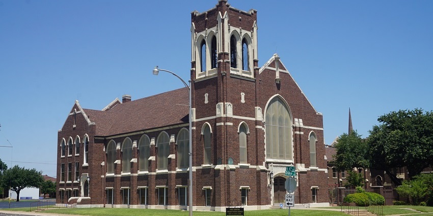 Tall stone church with arched windows, surrounded by trees under clear blue sky, one of the best things to see in Orange Texas.