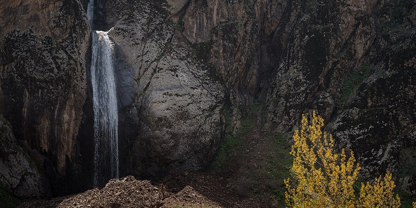 A narrow waterfall from rocky cliffs into a distant water body, hidden places to visit near Tashkent.