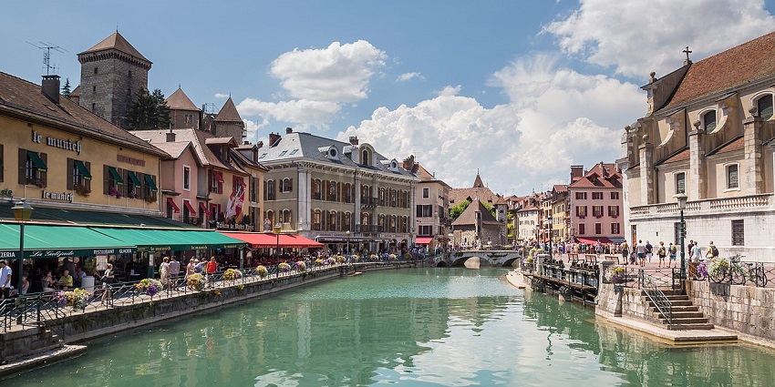 The scenic canal in Annecy, France, is lined with colorful buildings, cafes, and a vibrant crowd.