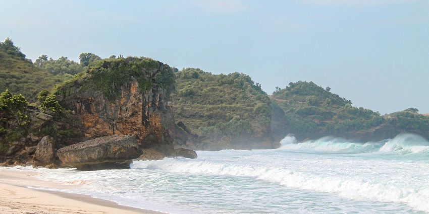 Waves crashing on the sandy shores of Anyer Beach under a sunny sky.
