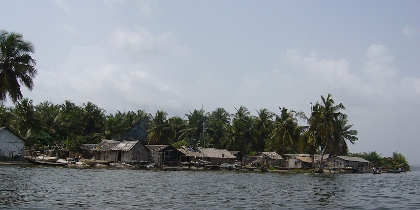 The shoreline of Île Napoléon in Assinie with palm trees and thatched huts near the water.