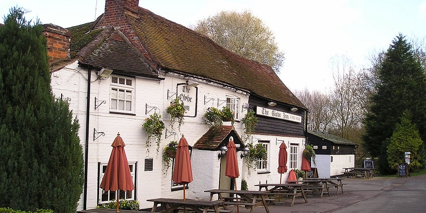 Exterior of a traditional British pub with signage, brick walls, and large front windows.
